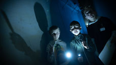 Synstolkning: tre barn med lommelykter på vei til kirketårnet.