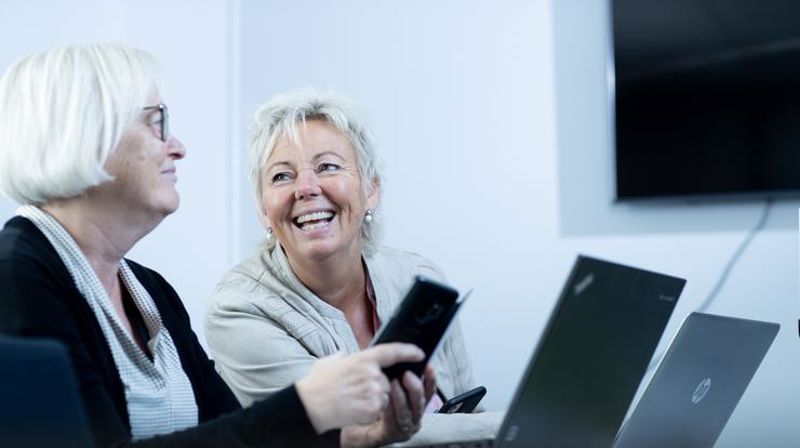 To personer smiler med en bærbar datamaskin foran seg