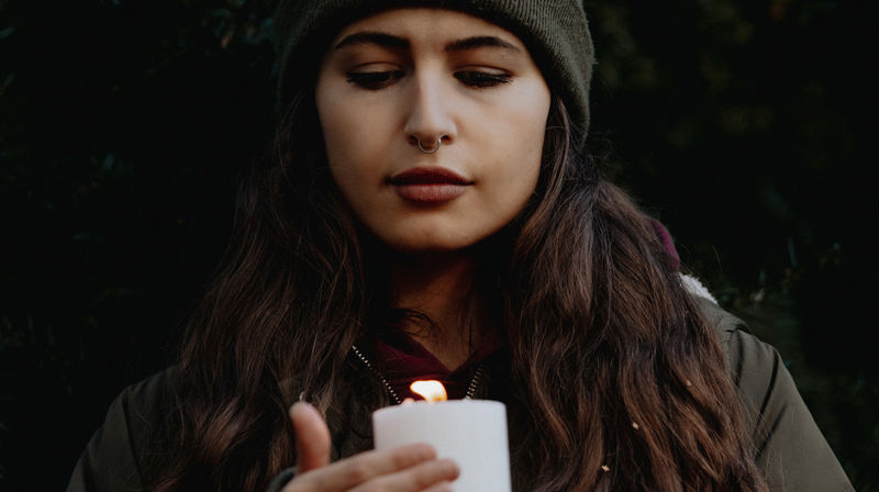 Ung kvinne står med et kubbelys i hendene. Hun kikker inn i flammen.