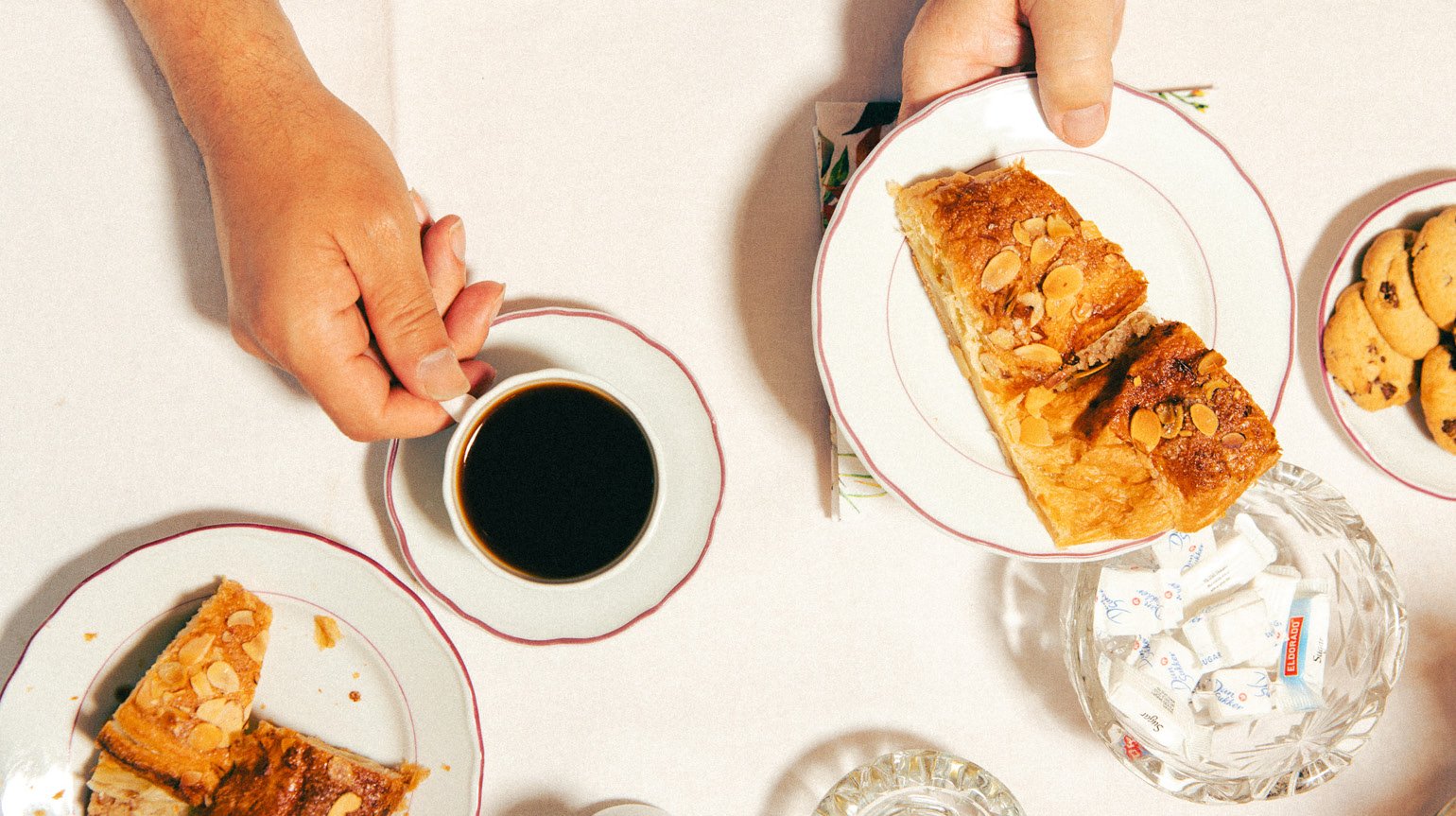 Et par hender holder fat med kaffe og kaker over et bord