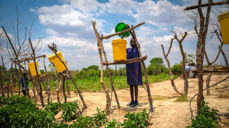 Ved hjelp av ganske små dropar vatn og dryppirrigasjon kan det vekse planter. Her fyller Prevencia frå Zambia vatn i bøtter, og vatnet blir ført ut gjennom tynne slangar til plantene. Foto: Kirkens nødhjelp