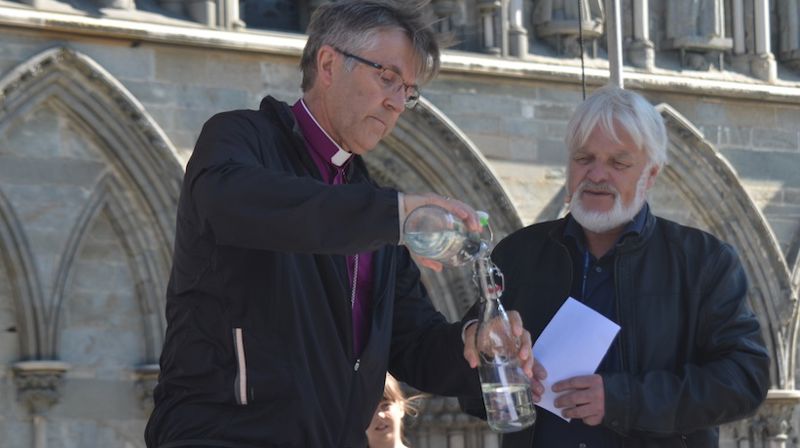 Tomm Kristiansen følger nøye med når biskop Tor Singsaas gjør klar flasken med vann som er på vei fra Svalbard til Klimatoppmøtet i Paris