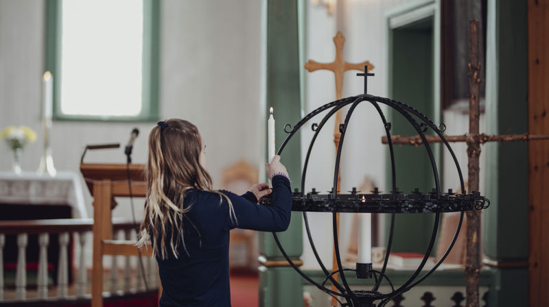 Jente plasserer et tent lys i lysgloben i Saltdal kirke. Foto: Frida Bringslimark
