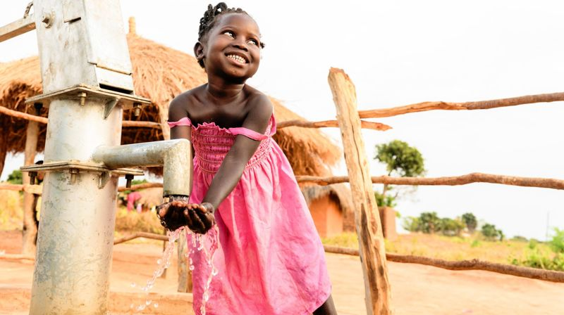 På bildet ser dere Champo. Ei 5 år gammel jente fra Zambia som får rent vann fra en av vannpumpene som Kirkens Nødhjelp har satt opp. Takket være denne vannpumpa holder familien seg friske. Mor har fått seg jobb – for hun trenger ikke lenger å gå dagslange turer for å hente vann, og Champo og søsknene kan være som barn og leke og gå på skole. Kirkens Nødhjelps arbeid nytter!