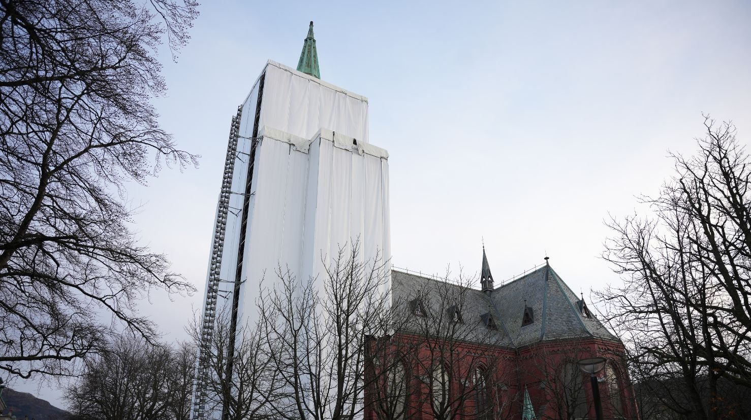 teglkirke med stillas og plast rundt tårnet. Foto.