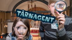 Bilde av to barn med forstørrelsesglass, en jente til venstre og en gutt til høyre. Midt på bildet er en logo med teksten "Tårnagent".