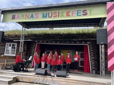 Brandbu Barnekantori og Kormix deltok under den store "Barnas Musikkfest" på Hadeland Folkemuseum i juni 2024. Her er de under fremføringen sammen med korleder Marit Wesenberg (foto: Anne-May Lervik). 