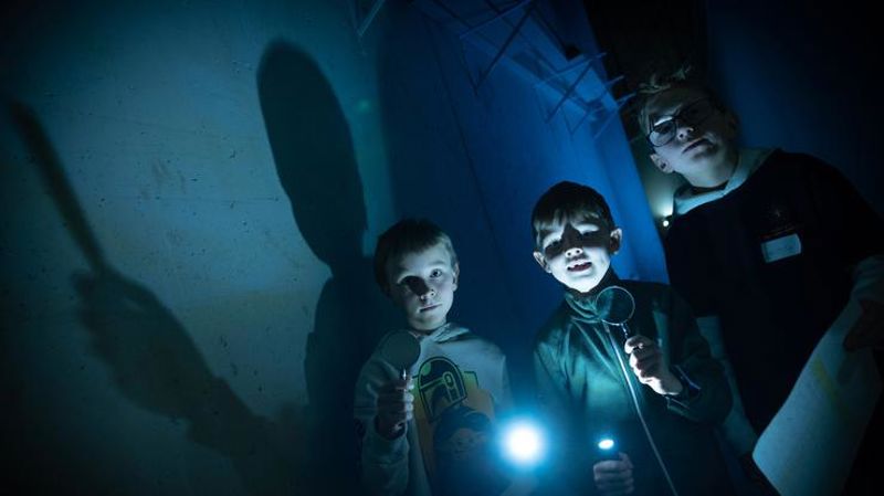 Bilde av tre barn som står i mørket. To av dem holder et forstørrelsesglass i den ene hånda og en tent lommelykt i den andre hånda. Foto: Sven Erling Brusletto