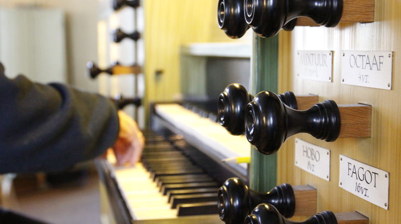 Nærbilde av registerknappene på et orgel i Fjell kyrkje, man kan se hender spille på tangentene i bakgrunne