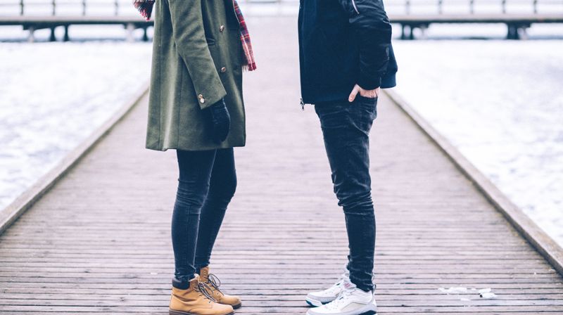 En dame og en mann står mot hverandre på en brygge, de går med jakker. 