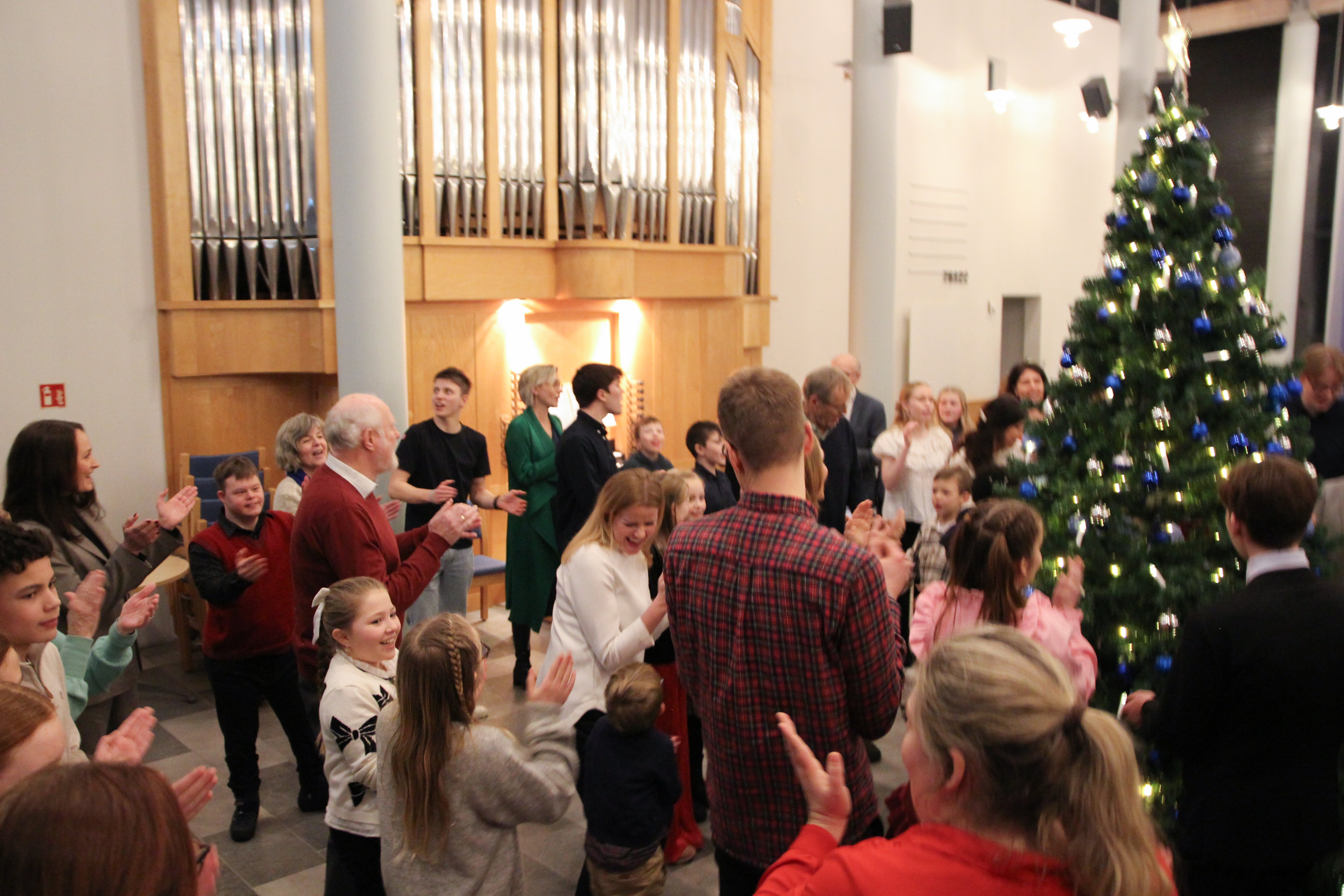 Mennesker går rundt juletre, de klapper til sangen