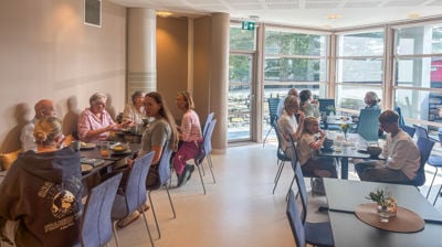 Mennesker sitter langs og ved bord og prater og spiser