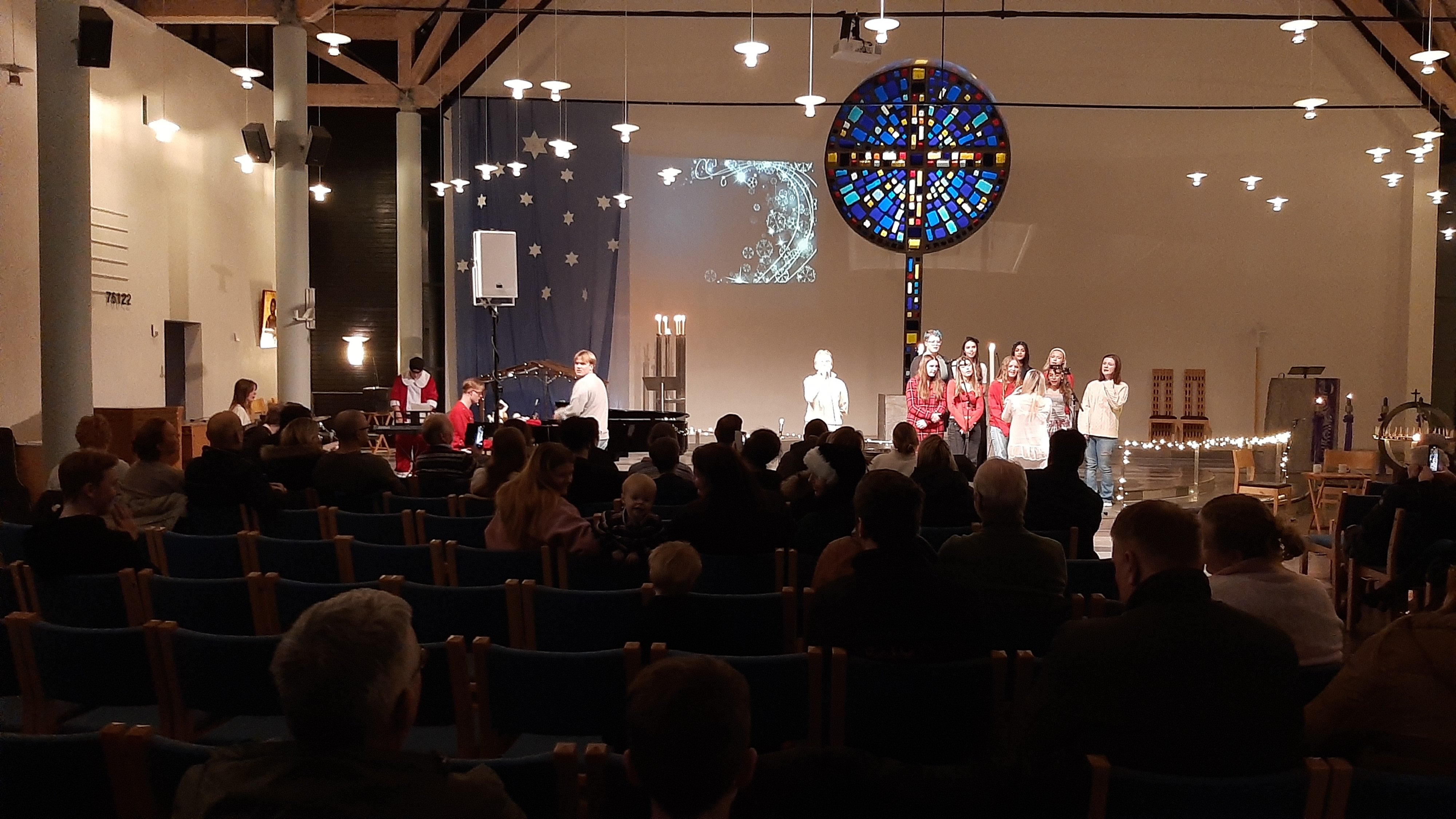 Ungdommer står fremme i kirken og synger, til venstre i bildet sitter noen og spiller ulike instrumenter