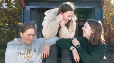 Tre jenter som sitter på en benk og smiler og prater