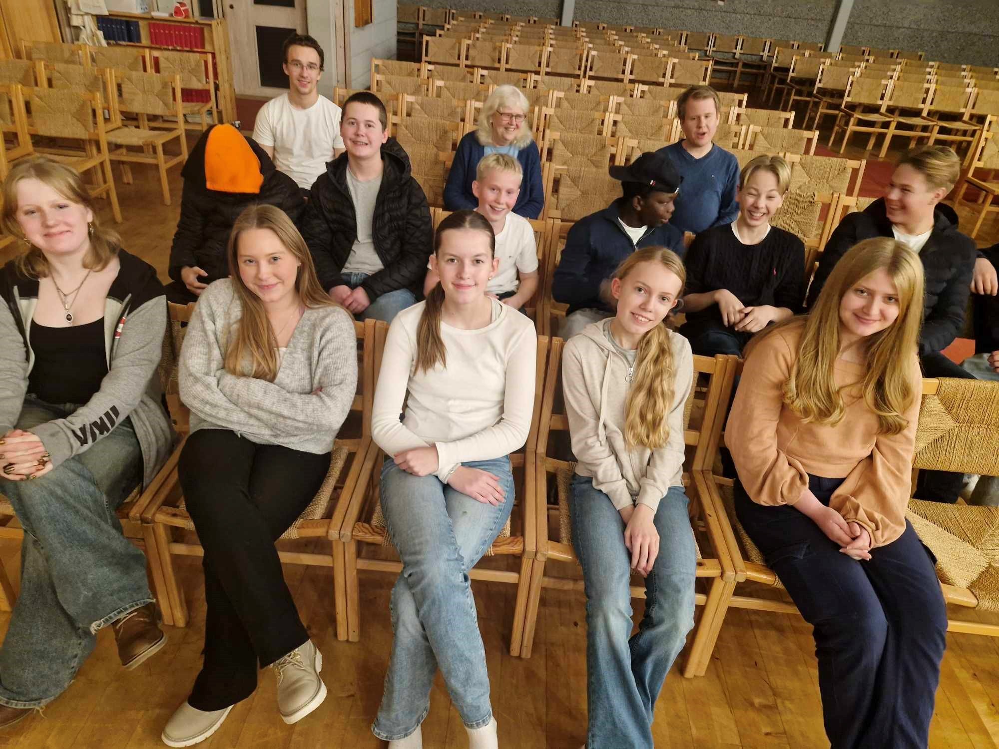 Ungdommer sitter på stoler i kirken og smiler til kameraet