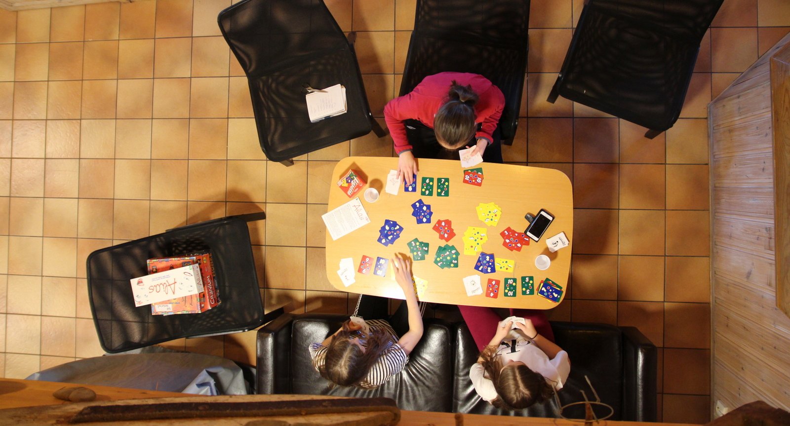 Sett ovenifra, ungdommer sitter på godstoler ved et bord og spiller kortspill