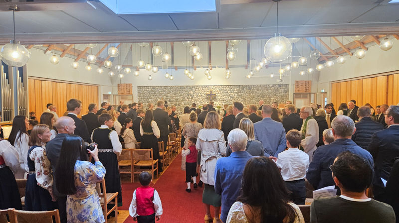 mennesker står i stolradene og ser på inngangsprosesjonen til gudstenesten